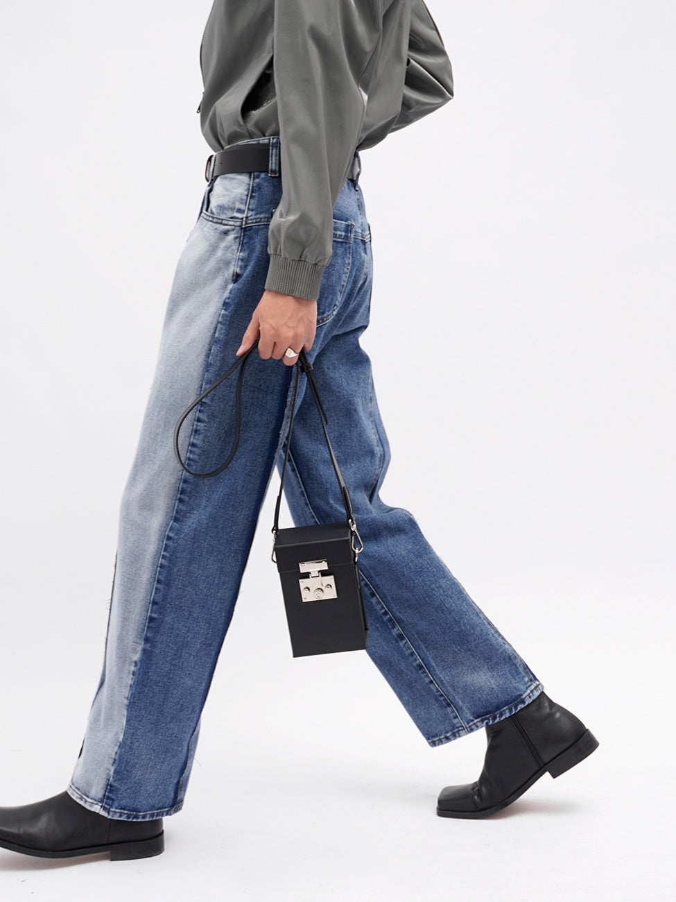Person wearing blue jeans and a green shirt, holding a black handbag on a white background