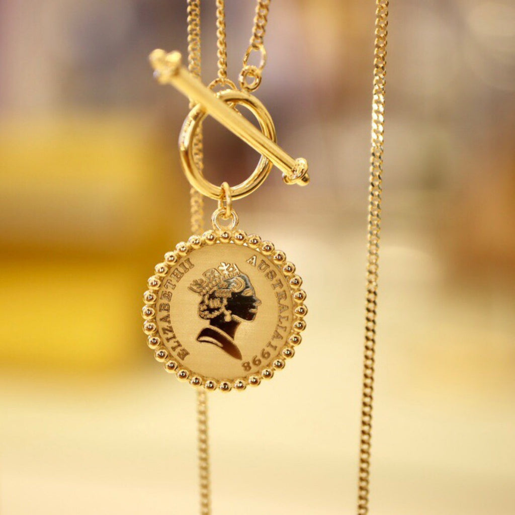 Gold necklace with a pendant featuring a profiled face design on a blurred gold background