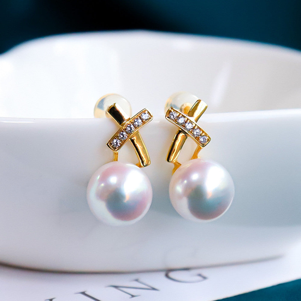 Pearl earrings with gold X-shaped designs on a white surface