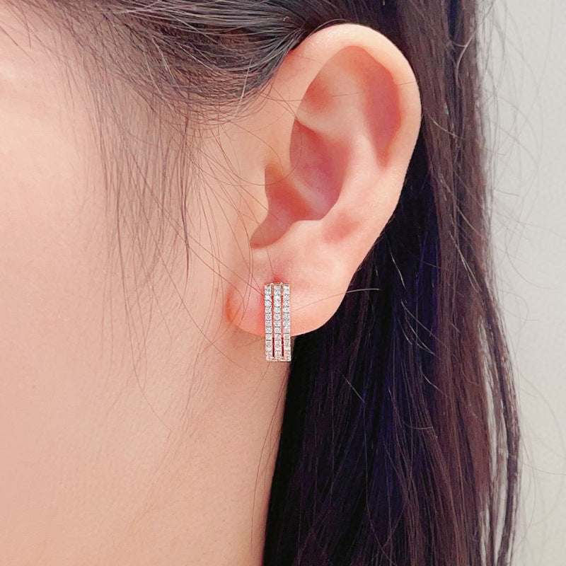 Close-up of an ear wearing a diamond hoop earring with a neutral background