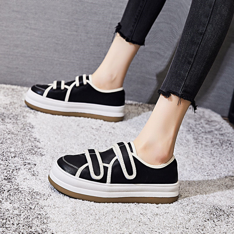 Black sneakers with white laces worn by a person on a textured surface.