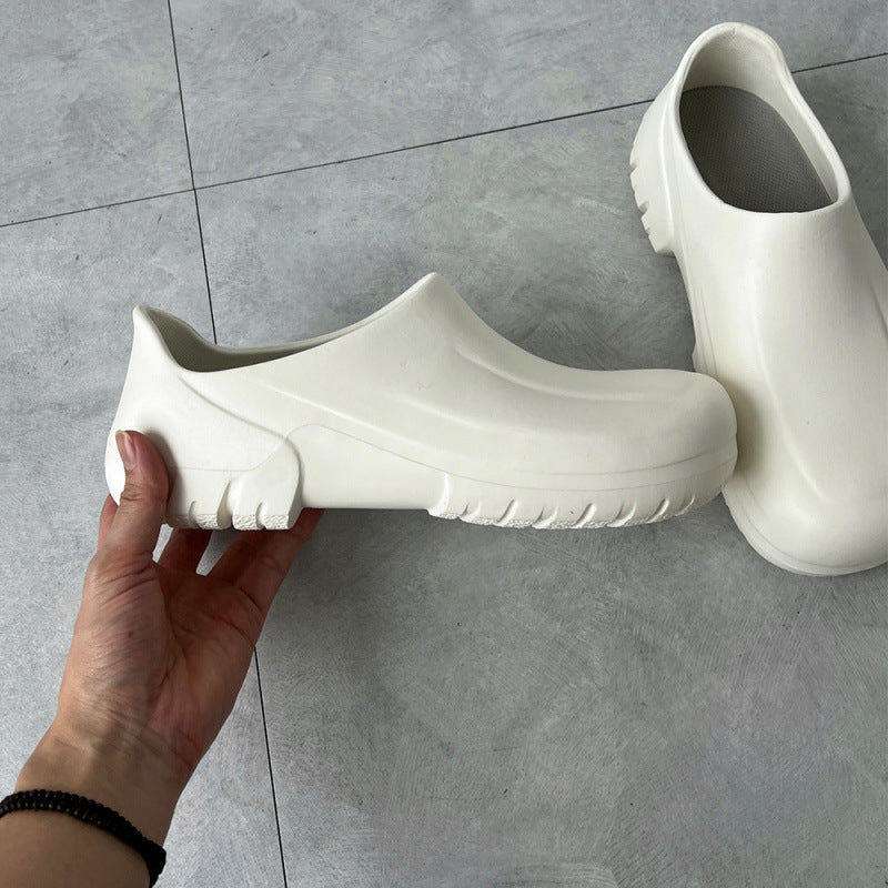 White clogs on a gray tiled floor with a hand holding one shoe.