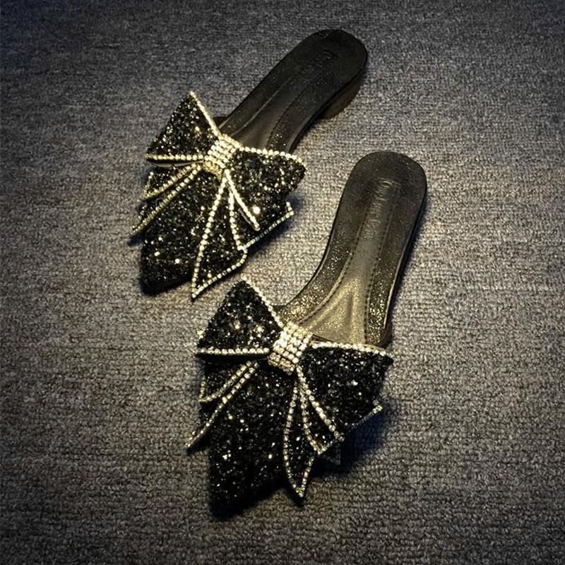 Black slippers with decorative bows on a dark textured surface