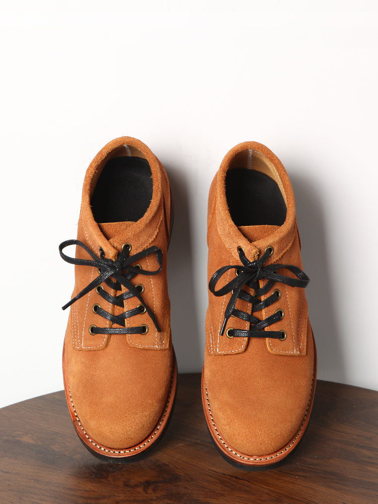 Pair of brown leather shoes with black laces on a wooden surface.
