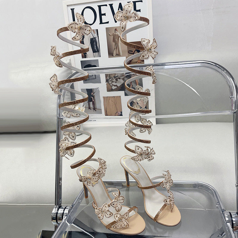 Pair of high-heeled shoes with decorative straps on a clear stand.