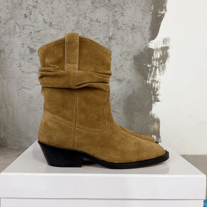 Tan suede boot on a white pedestal with a textured gray wall background