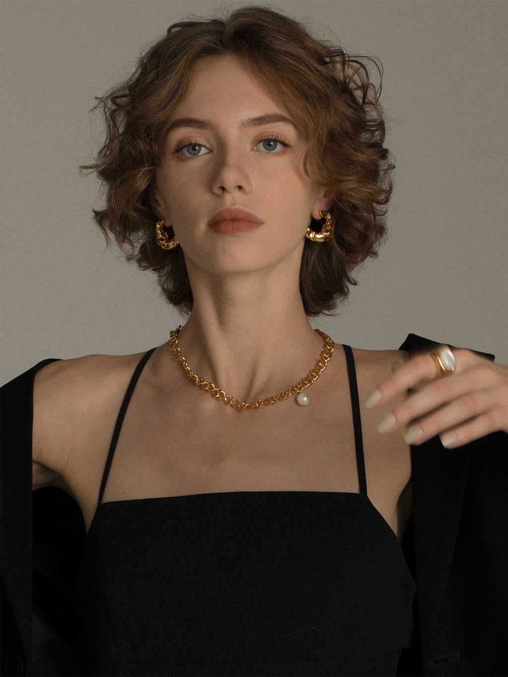 Woman wearing a black top and gold jewelry against a neutral background