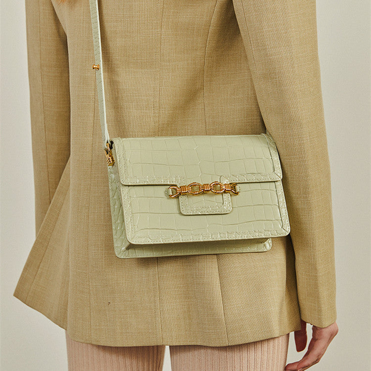 Person wearing a beige suit with a light green handbag featuring a gold chain detail.