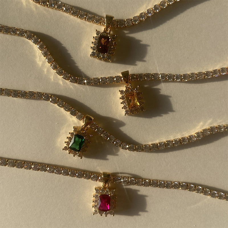 Gold necklaces with gemstone pendants on a beige surface