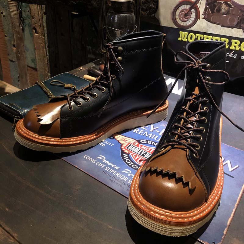 Pair of black and brown leather boots on a wooden surface with a motorcycle-themed magazine in the background.