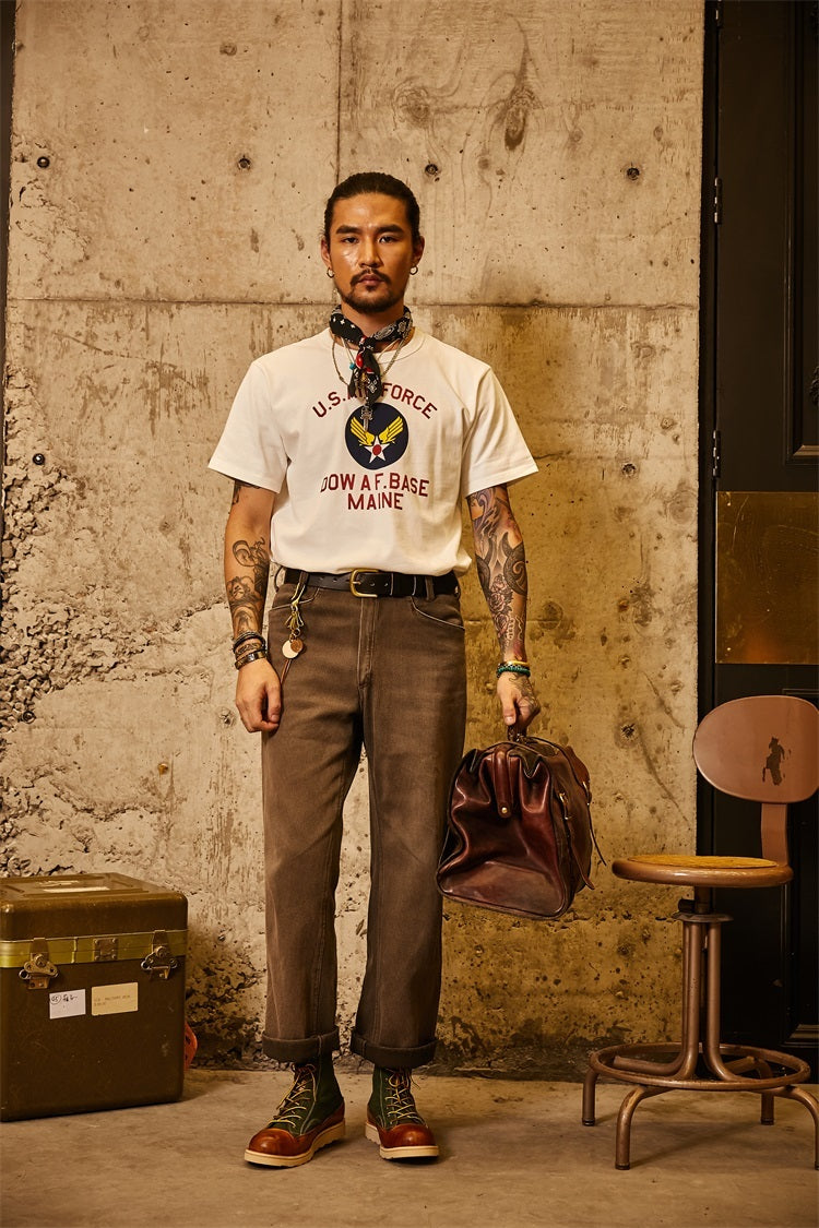 Man in vintage-style clothing holding a leather bag against a textured wall.