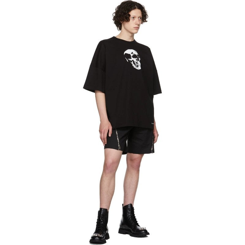 Person wearing a black t-shirt with a skull design and black shorts on a white background
