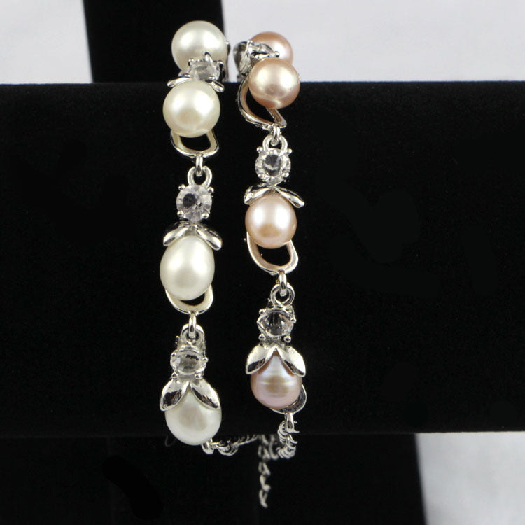 Pearl and crystal drop earrings on a black stand with a white background