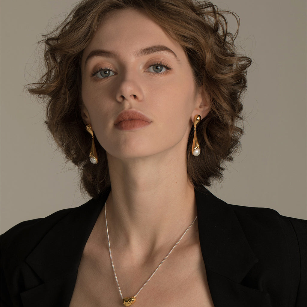 Woman wearing gold earrings and a necklace against a neutral background