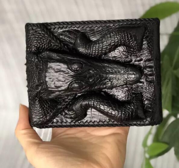 Black leather wallet with embossed alligator design held by a hand against a light background.