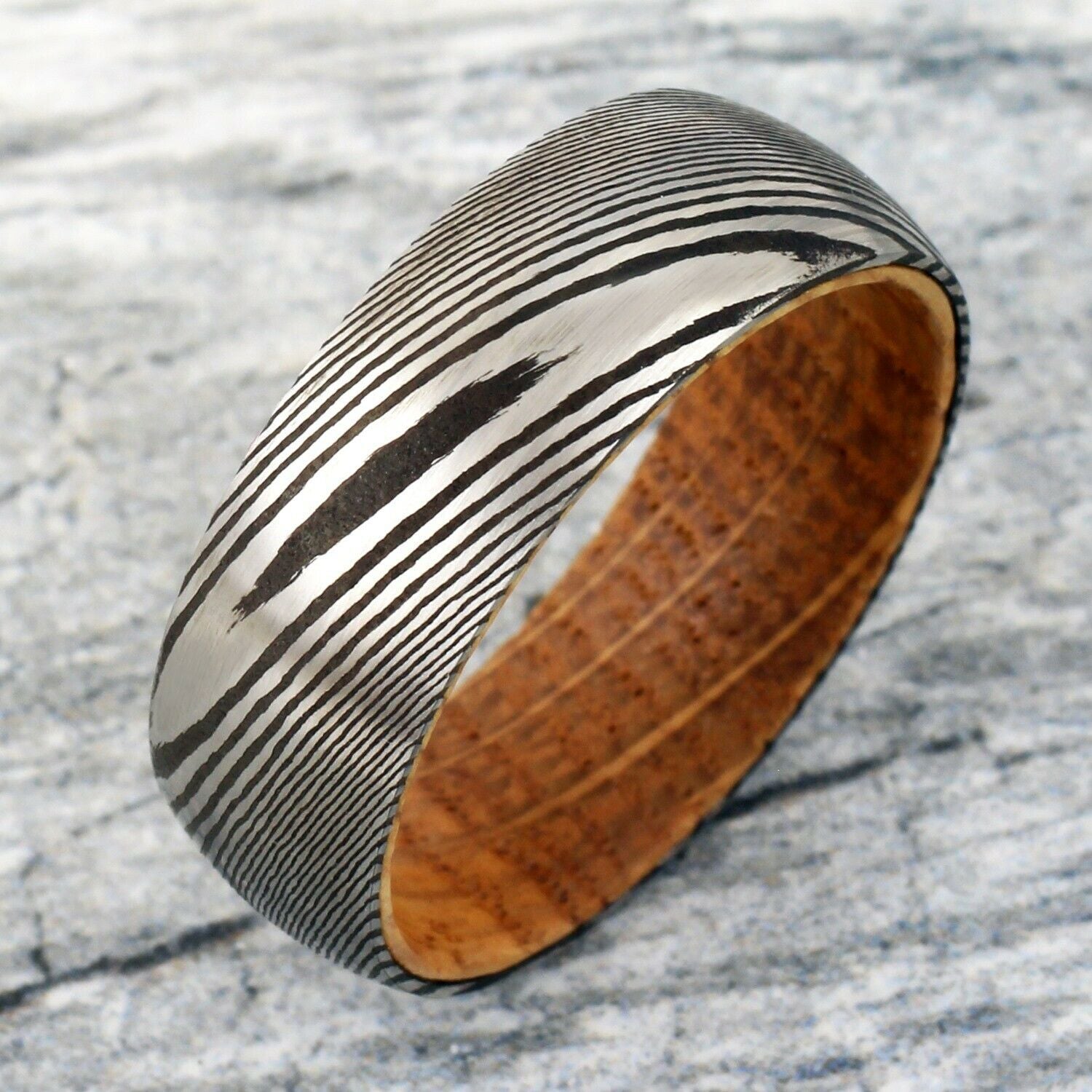 Damascus steel and wood ring on a textured surface