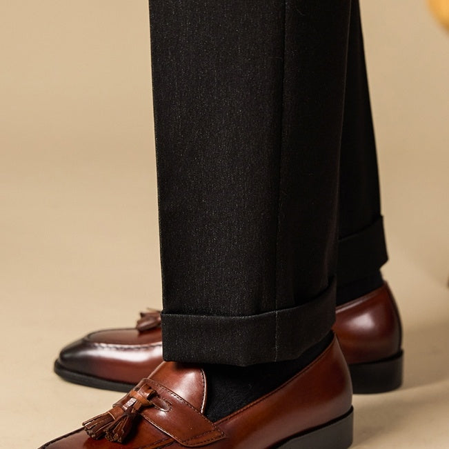 Brown loafers with tassels worn with black pants on a beige background