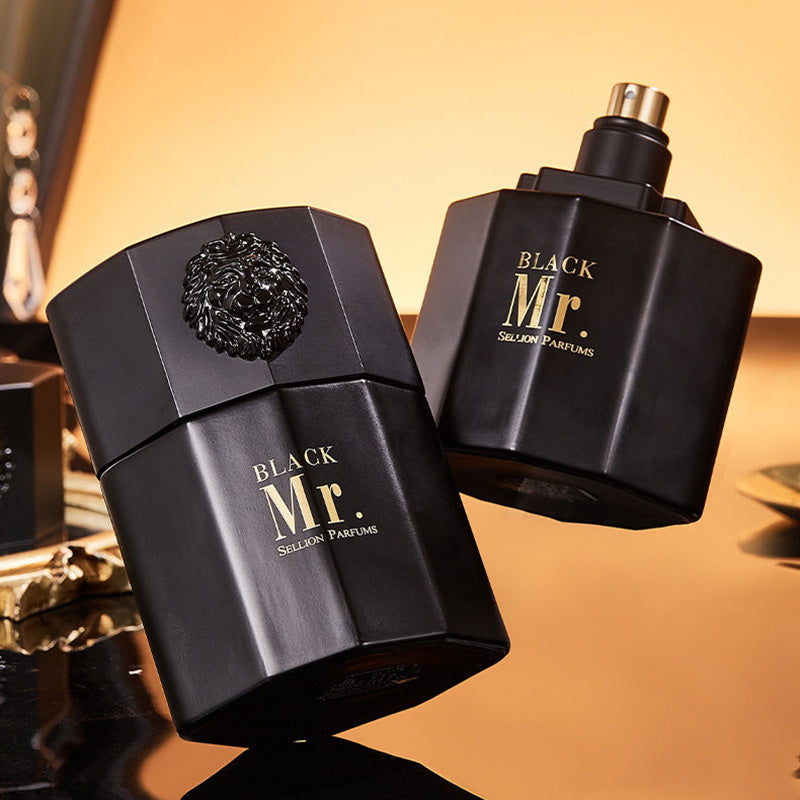 Two black 'Black Mr.' perfume bottles on a reflective surface with a warm background.