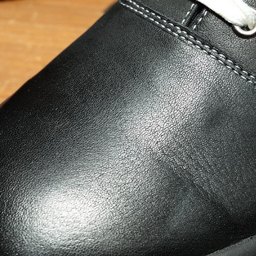 Close-up of a black leather shoe with visible scuff mark on a wooden surface