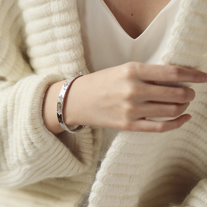 Close-up of a hand wearing a silver bracelet against a neutral background