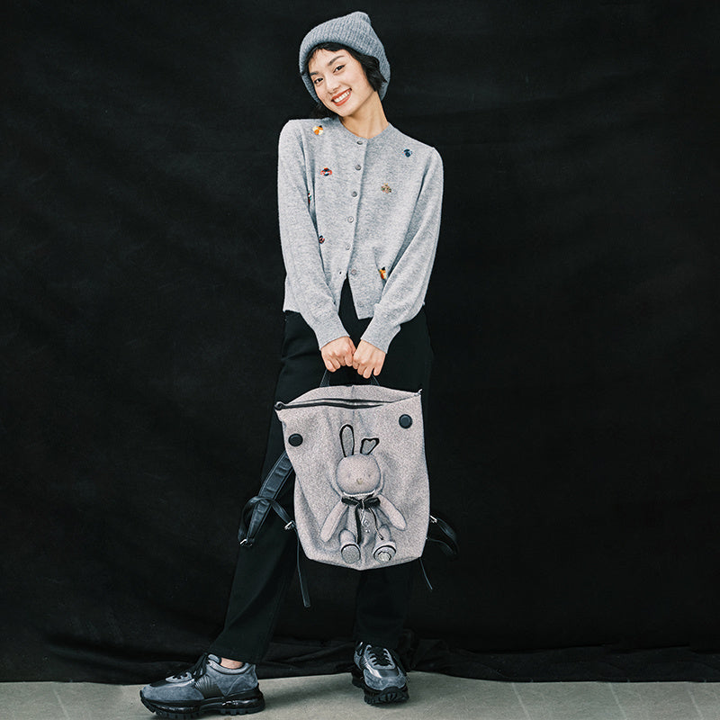 Person holding a gray backpack with a cartoon design against a black background