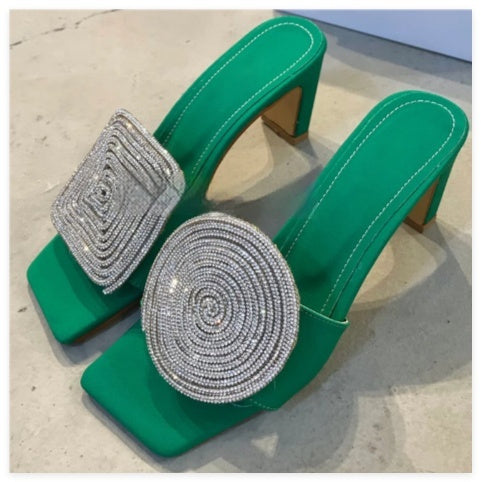 Green high-heeled shoes with silver embellishments on a light background