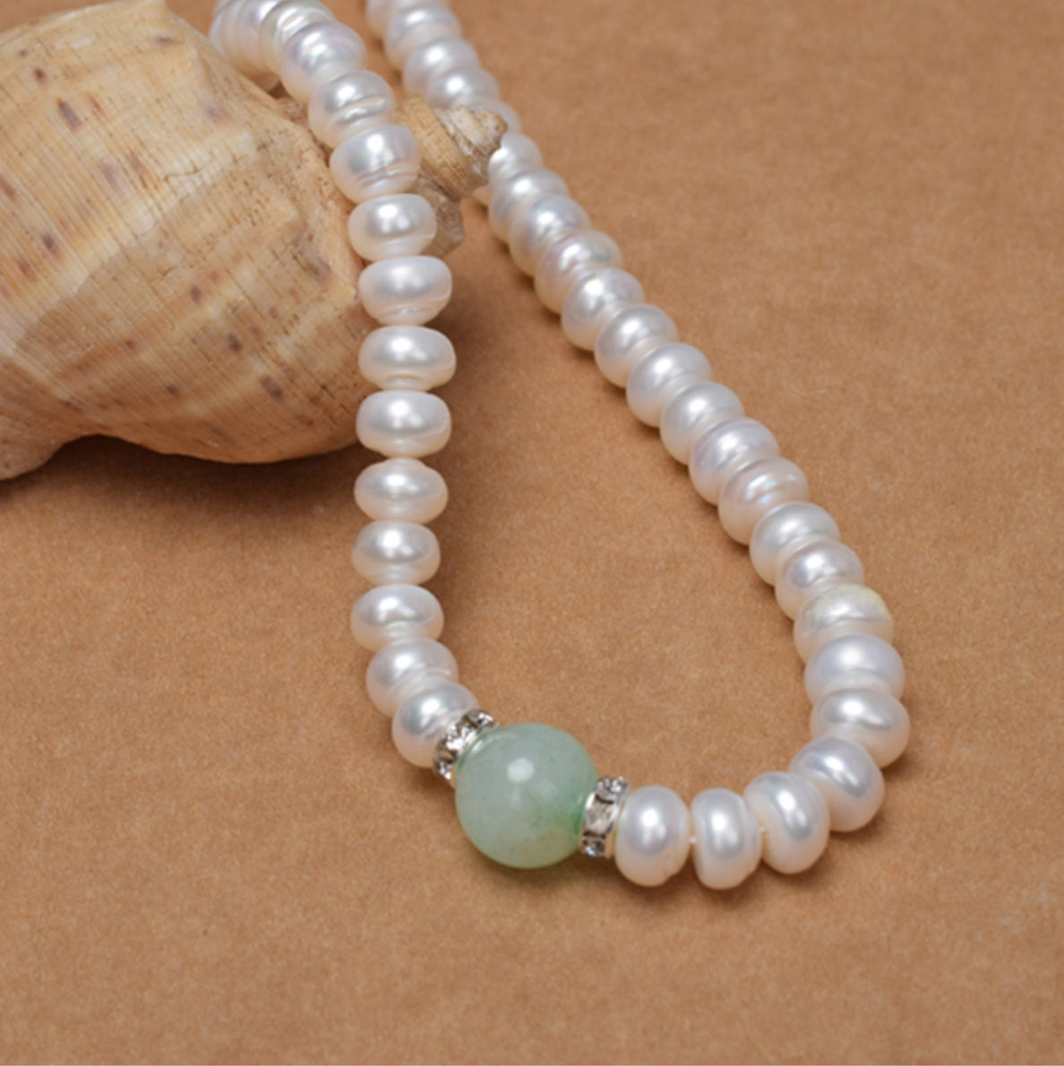 Pearl necklace with a green bead and silver clasp on a brown background