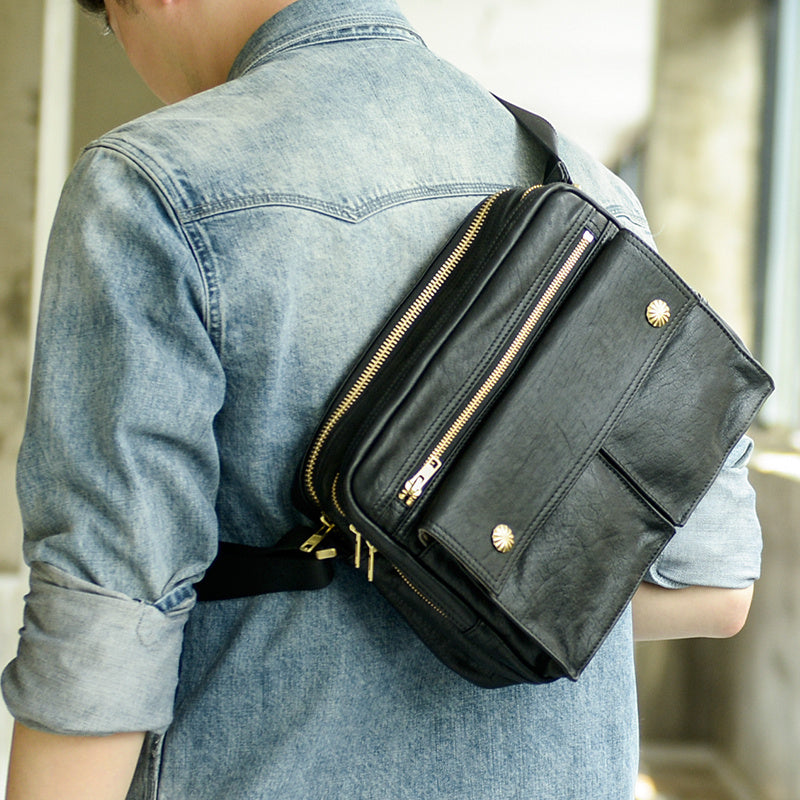 Person wearing a black leather crossbody bag with gold zippers.