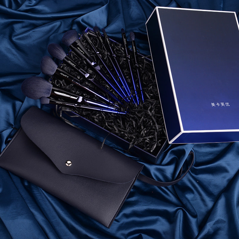 Set of makeup brushes in a box with a black clutch on a blue fabric background