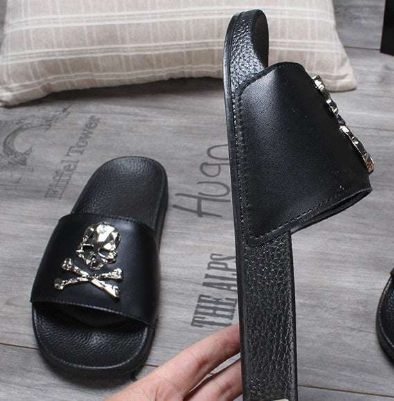 Black slide sandal with skull design on a wooden floor