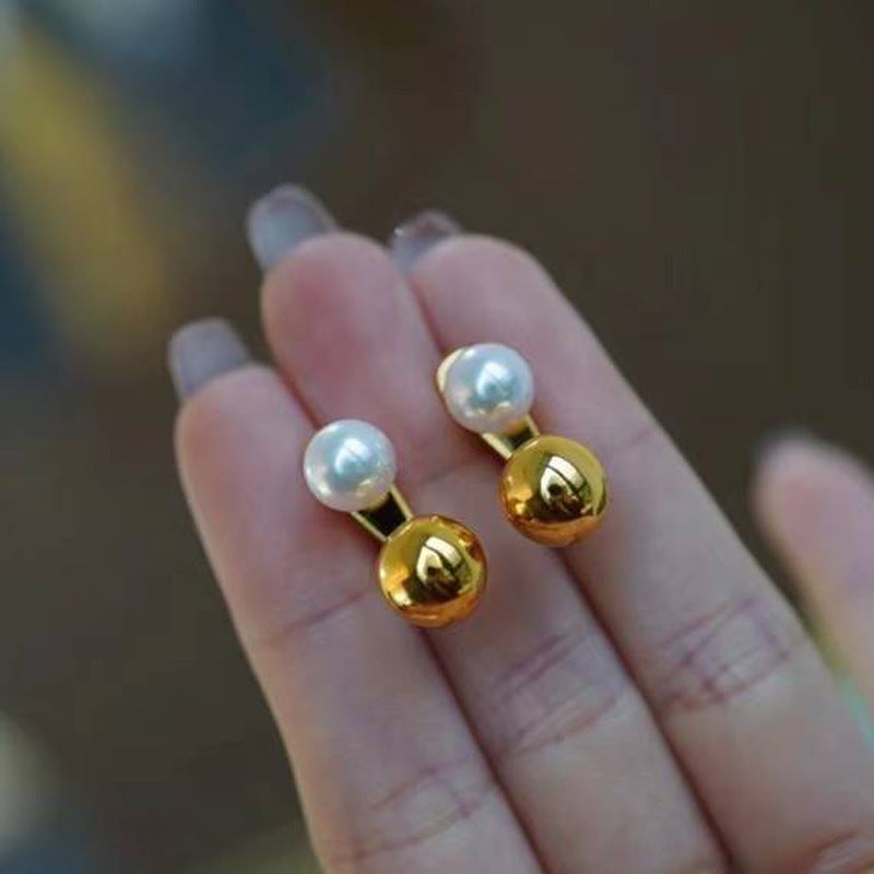 Gold and pearl earrings held on a hand with a blurred background