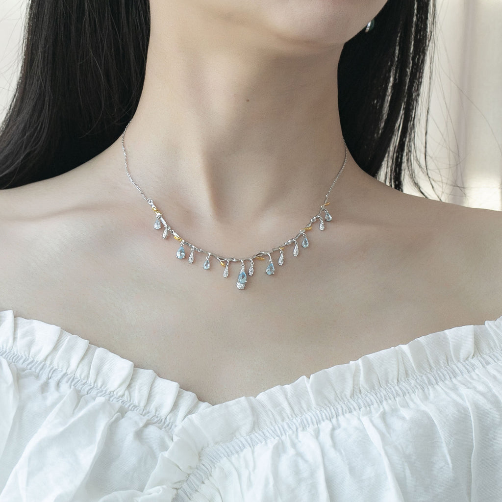 Necklace with small, multicolored stones worn by a person in a white top.