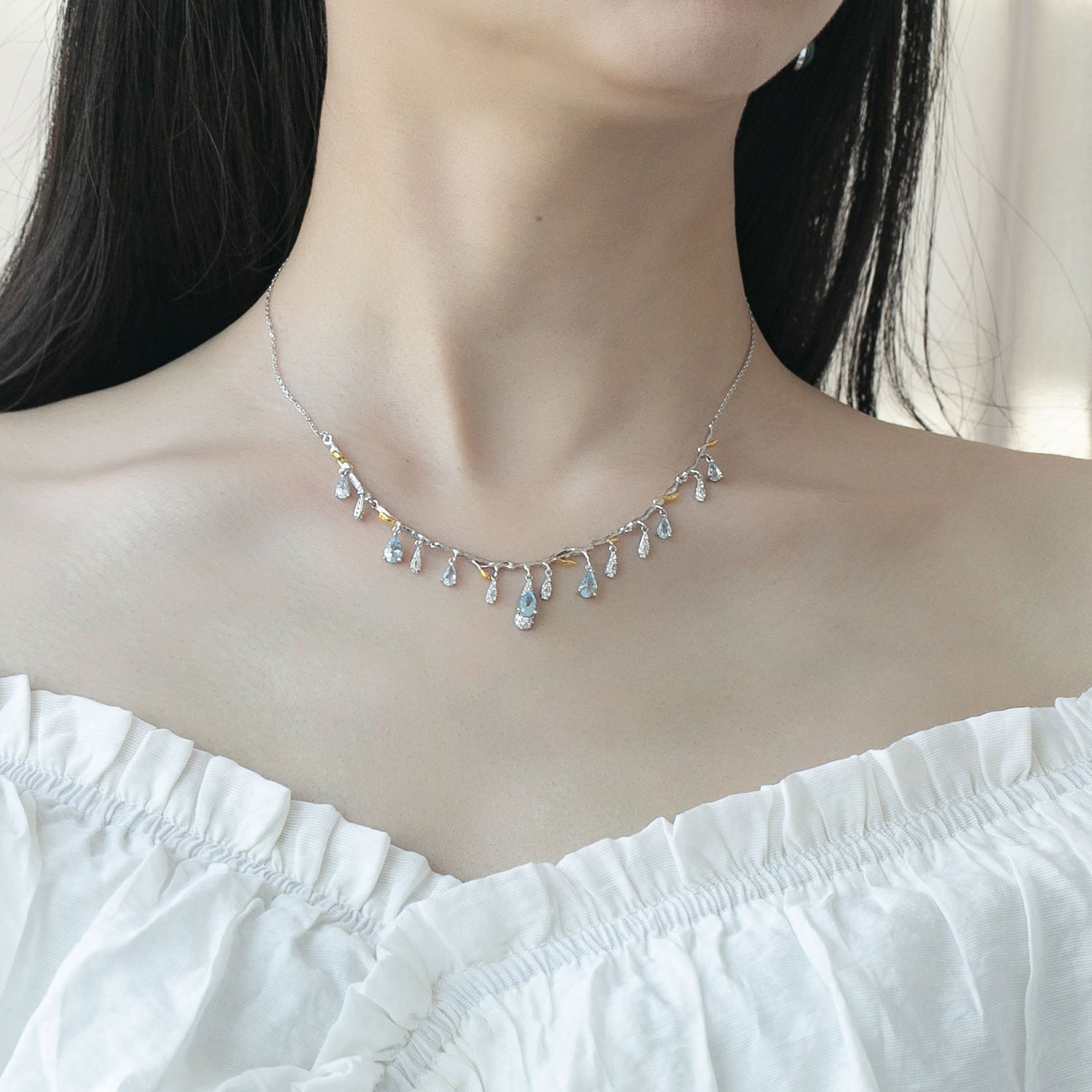 Necklace with small, multicolored stones worn by a person in a white top.