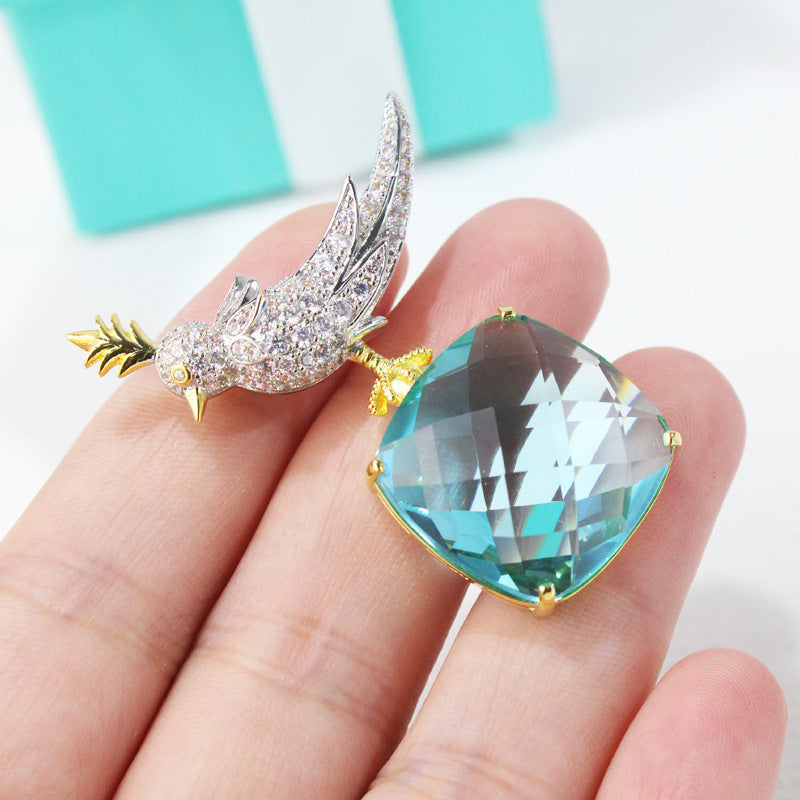 Earring with blue teardrop gemstone held between fingers against a light background