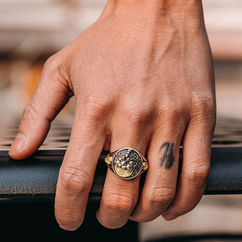 Hand wearing a gold ring with intricate design on a blurred background