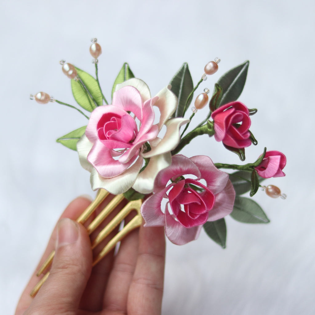Hair comb with pink and white floral design held by a hand against a light background