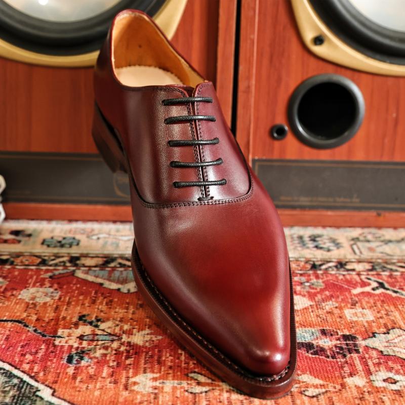 Brown leather dress shoe with black laces on a patterned rug with a wooden speaker in the background