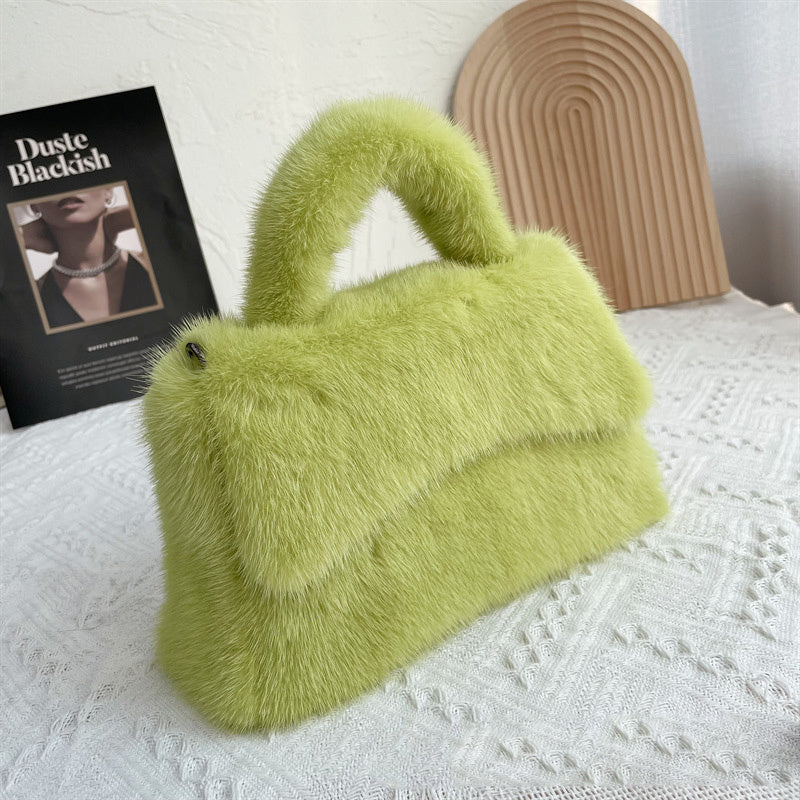 Green fluffy handbag on a textured surface with a book in the background