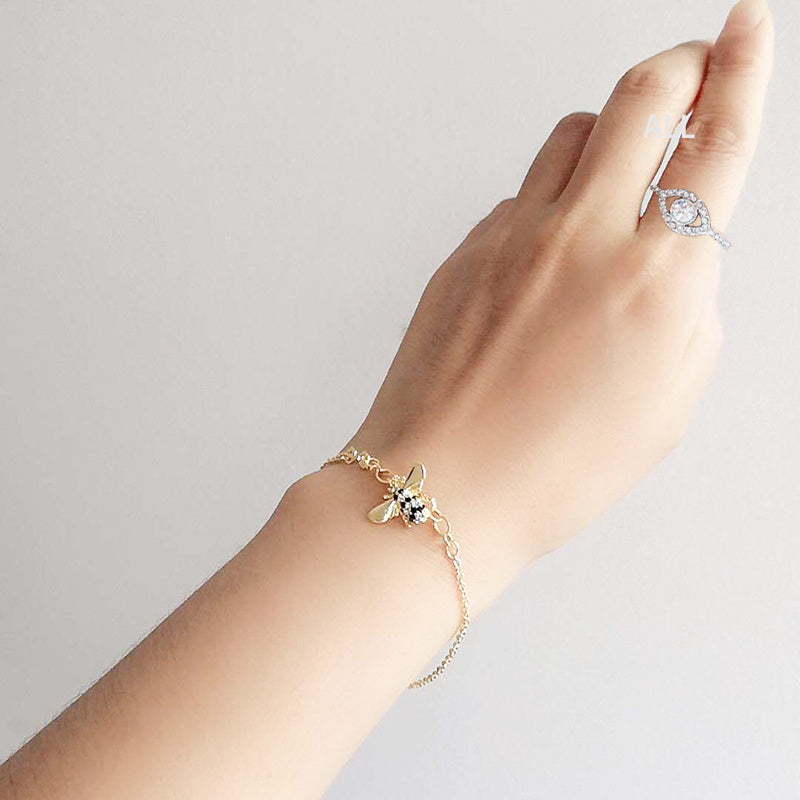 Hand wearing a gold bracelet with a bee design on a light gray background