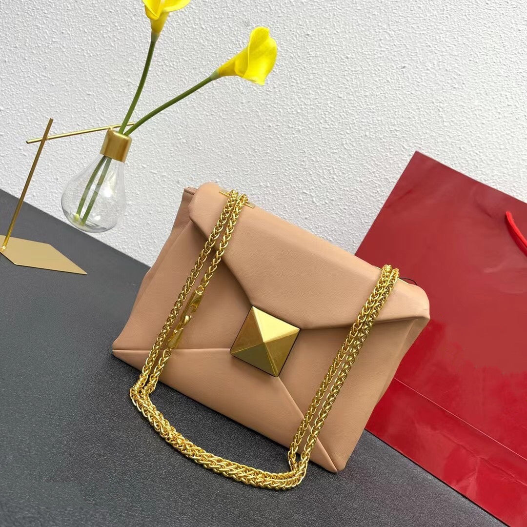 Beige handbag with gold chain and geometric detail on a gray surface with yellow flowers and a red bag in the background.
