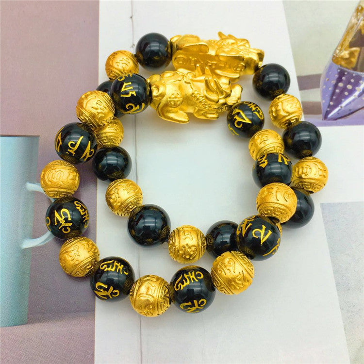 Bracelet with black and gold beads and a gold charm on a white surface.