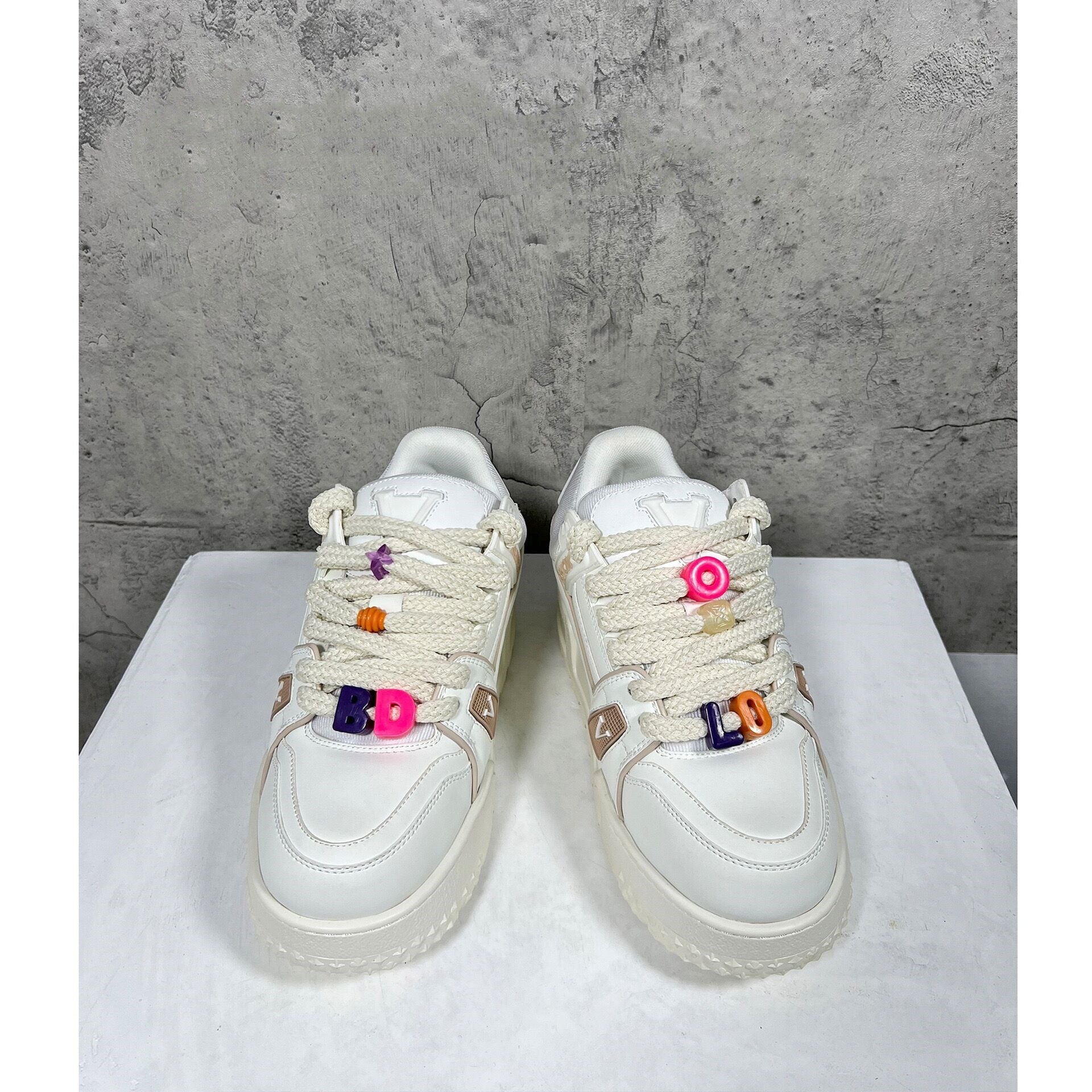 White sneakers with colorful accents on a white platform against a gray concrete wall.