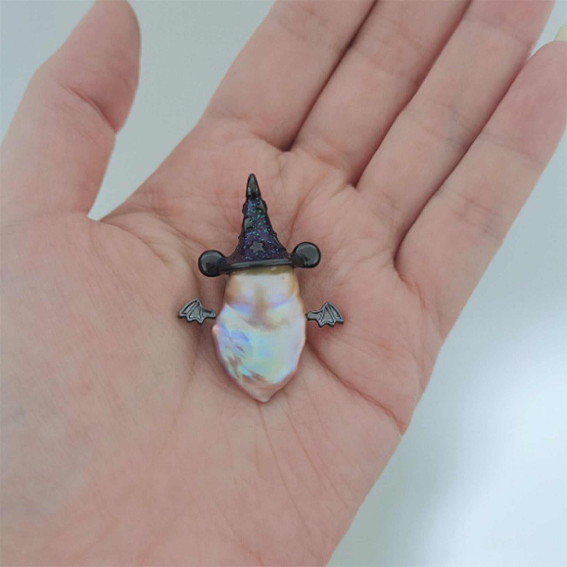 Pearl earring with a black hat design held in a hand against a white background