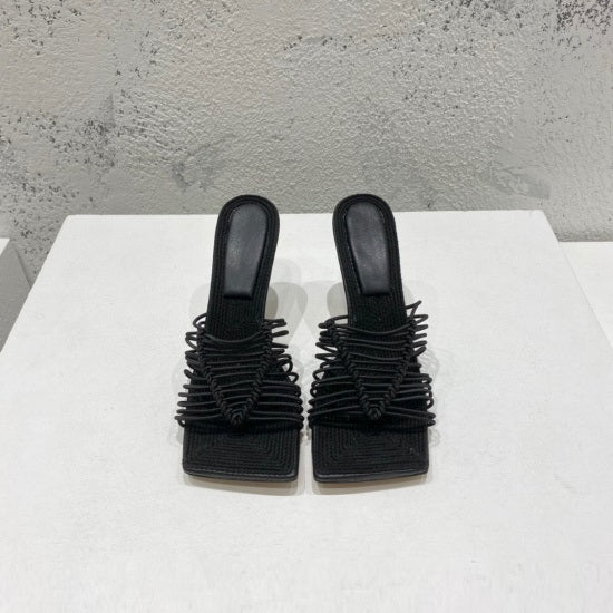 Pair of black strappy sandals on a white surface with a gray textured background