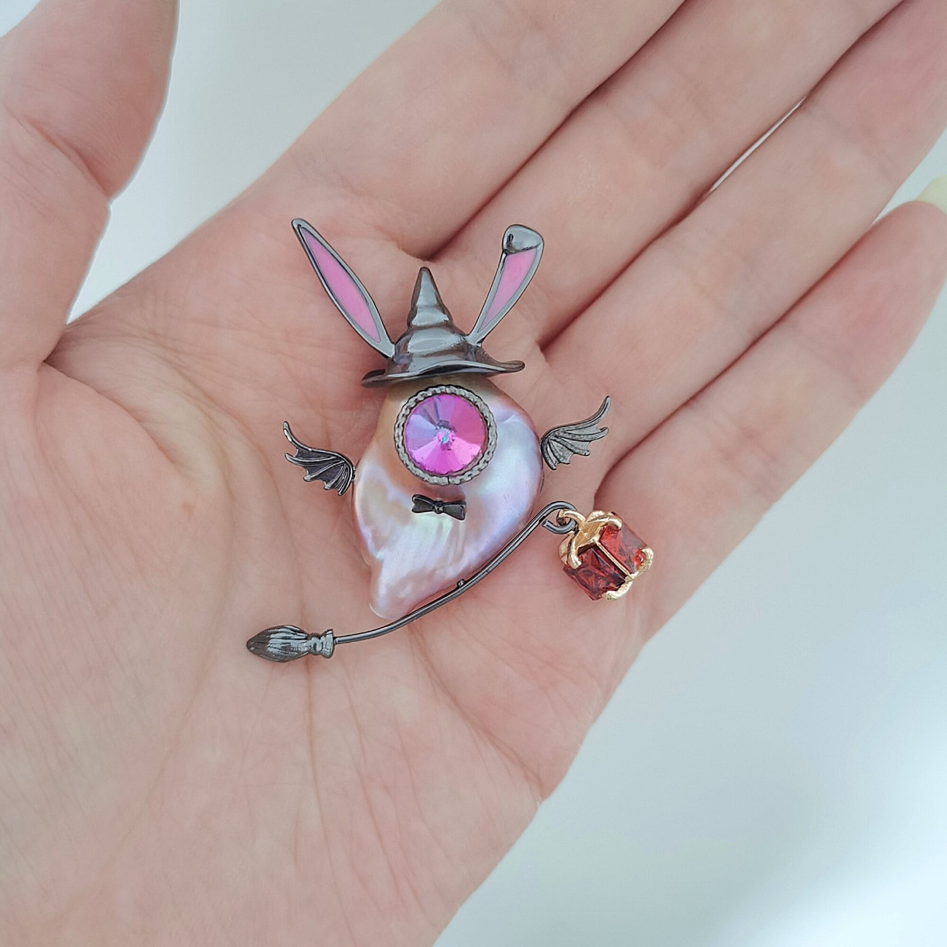 Decorative brooch resembling a rabbit with a pink gemstone held in a hand.