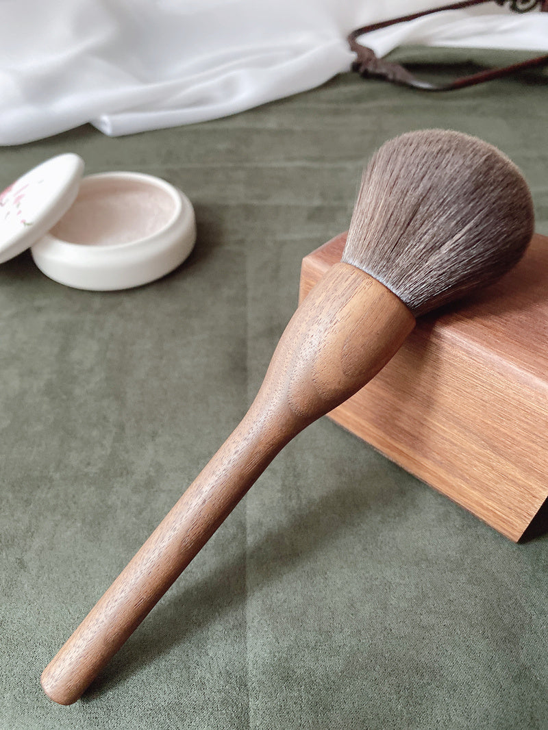 Makeup brush with wooden handle and natural bristles on a green surface