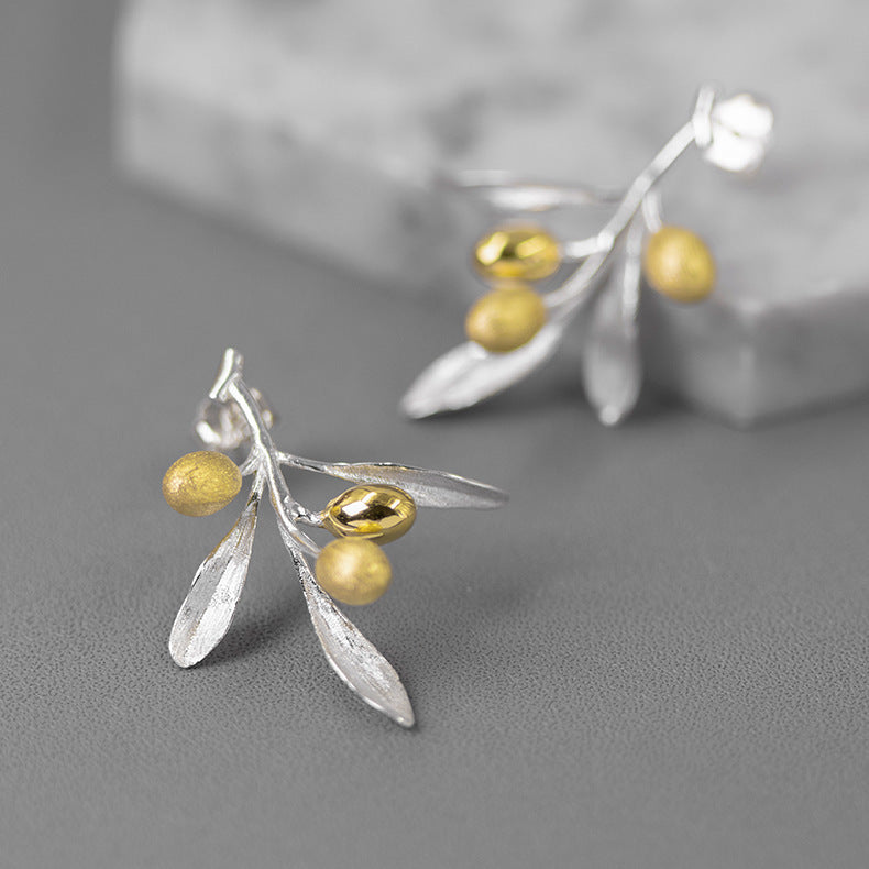 Silver and gold leaf earrings on a gray background