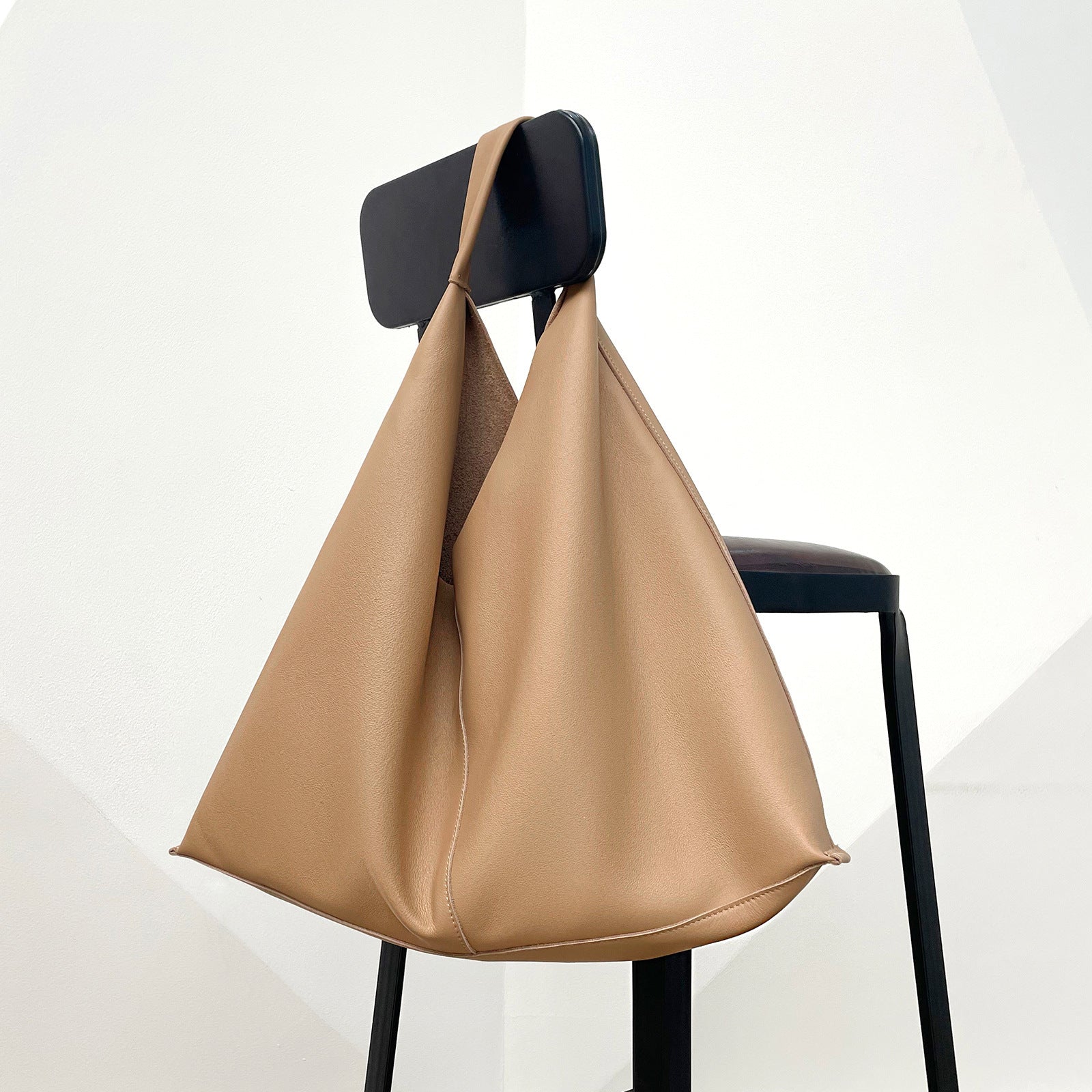 Beige handbag hanging on a black chair against a white background
