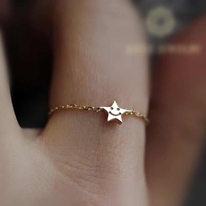 Gold star-shaped ring with a smiley face on a finger against a blurred background