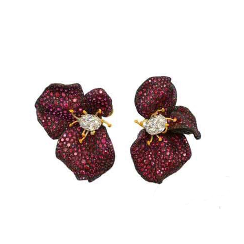 Pair of floral earrings with red gemstones and gold accents on a white background